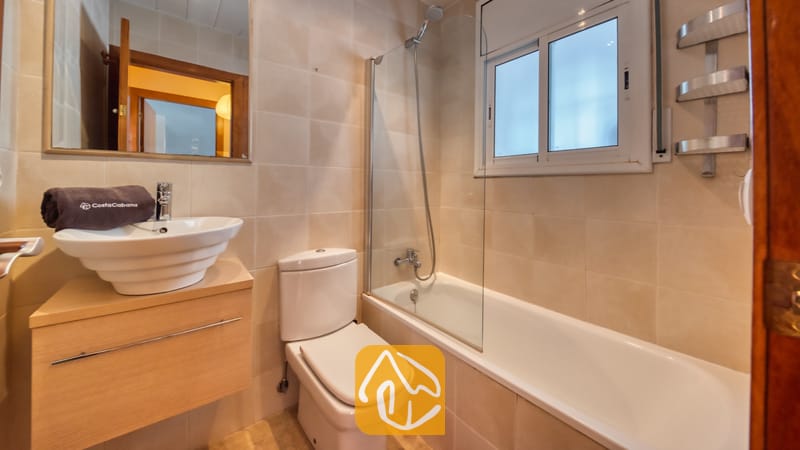 Villas de vacances Costa Brava Espagne - Villa Sofia - Salle de bains carrelée comprenant une baignoire blanche, une paroi de douche en verre, des toilettes et un meuble sous-lavabo moderne avec une serviette grise.