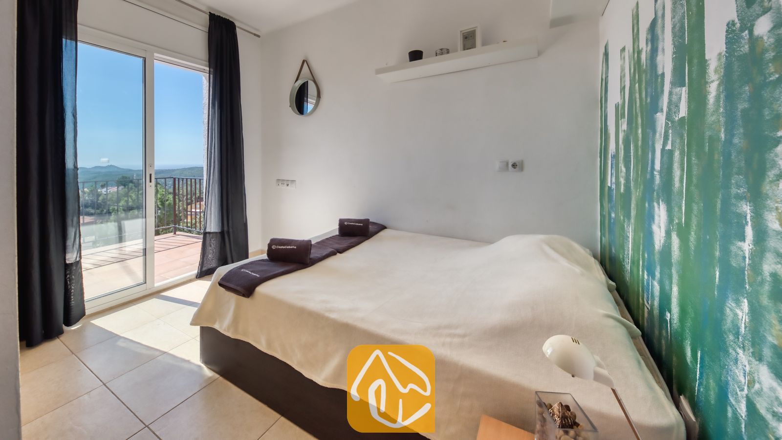 Vakantievilla's Costa Brava Spanje - Villa Sofia - Slaapkamer met een tweepersoonsbed, een wit-met-groen geschilderd accentmuur en een glazen schuifpui die toegang biedt tot een balkon.