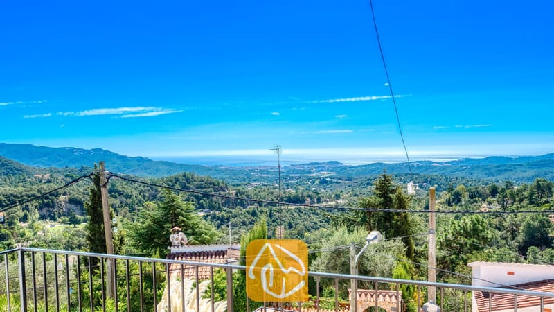 Vakantievilla's Costa Brava Spanje - Villa Sofia - Uitzicht vanaf het balkon van Villa Sofia op de groene heuvels, boomtoppen en de verre zee onder een helderblauwe hemel