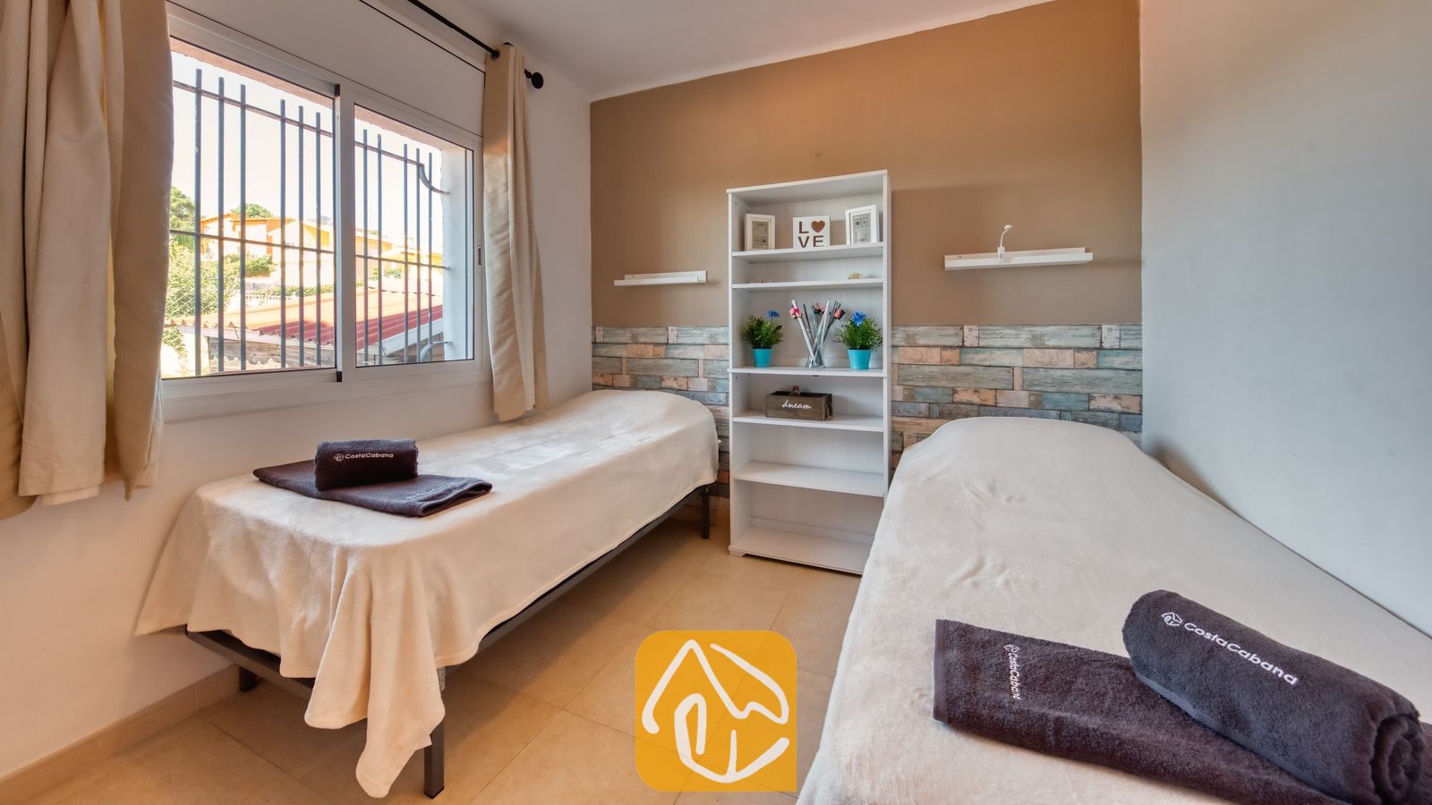 Vakantievilla's Costa Brava Spanje - Villa Sofia - Tweepersoonsslaapkamer in Villa Sofia met twee eenpersoonsbedden, donkerbruine handdoeken, een witte kast en een raam met beveiligingsroosters.