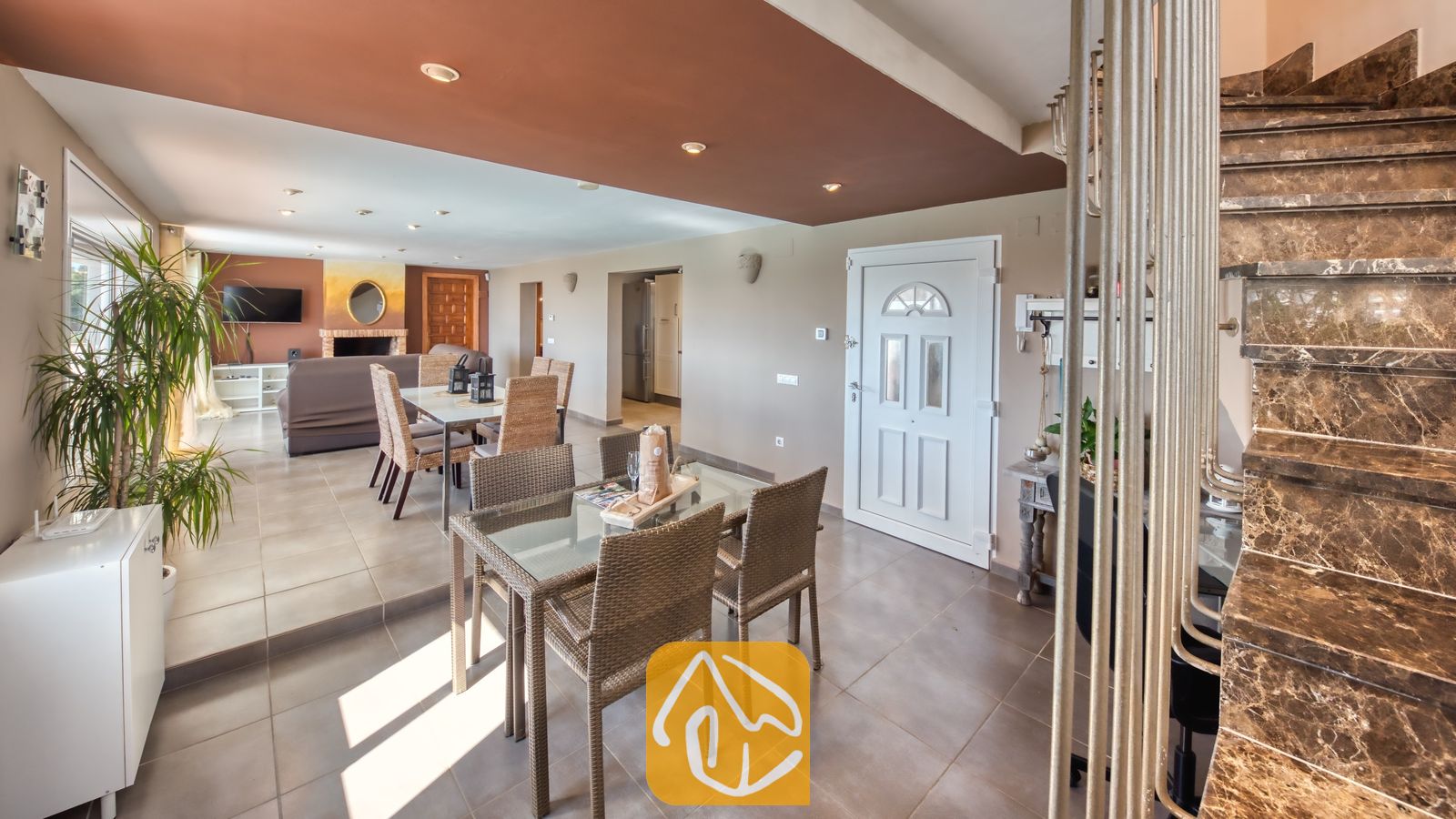 Vakantievilla's Costa Brava Spanje - Villa Sofia - Het ruime interieur van Villa Sofia, met een marmeren trap, twee glazen eettafels met gevlochten stoelen en een zitgedeelte op de achtergrond.