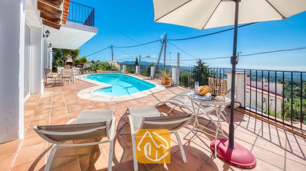 Vakantievilla's Costa Brava Spanje - Villa Sofia - Terras bij Villa Sofia met ligstoelen, een parasol, een kleine ronde tafel met een drankje en een buitenzwembad tegen een blauwe hemel.