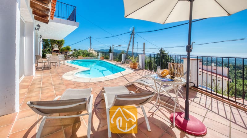 Vakantievilla's Costa Brava Spanje - Villa Sofia - Terras bij Villa Sofia met ligstoelen, een parasol, een kleine ronde tafel met een drankje en een buitenzwembad tegen een blauwe hemel.