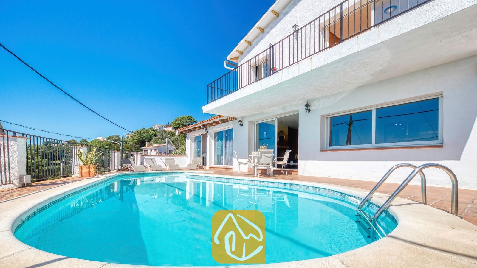 Vakantievilla's Costa Brava Spanje - Villa Sofia - Gebogen buitenzwembad met helderblauw water en metalen handgrepen voor de witte buitenkant van Villa Sofia onder een strakke blauwe lucht
