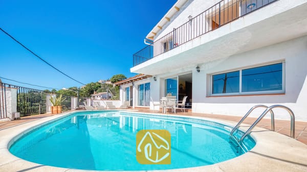 Vakantievilla's Costa Brava Spanje - Villa Sofia - Gebogen buitenzwembad met helderblauw water en metalen handgrepen voor de witte buitenkant van Villa Sofia onder een strakke blauwe lucht