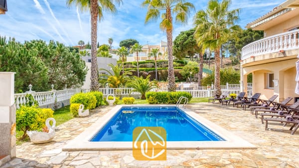 Vakantievilla's Costa Brava Spanje - Villa Estrella - Privézwembad bij Villa Estrella, omringd door een stenen terras, palmbomen, ligstoelen en prachtig onderhouden groene struiken onder een blauwe hemel.