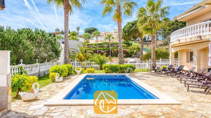 Vakantievilla's Costa Brava Spanje - Villa Estrella - Privézwembad bij Villa Estrella, omringd door een stenen terras, palmbomen, ligstoelen en prachtig onderhouden groene struiken onder een blauwe hemel.