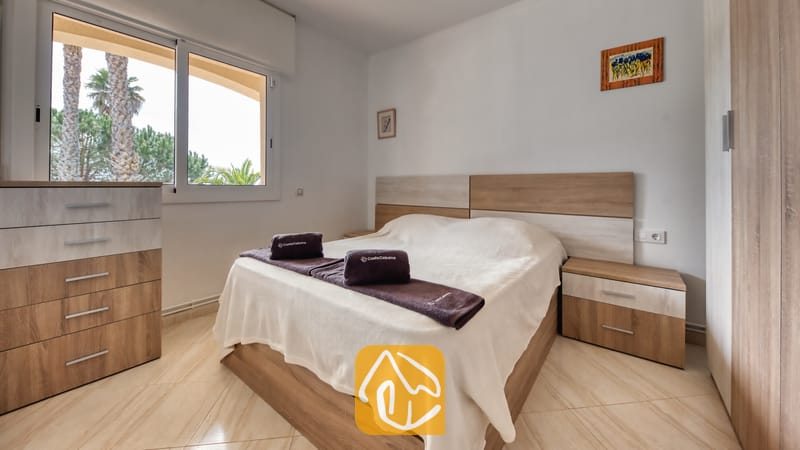 Villas de vacances Costa Brava Espagne - Villa Estrella - Chambre avec un lit double, des meubles en bois clair et une fenêtre donnant sur des palmiers.