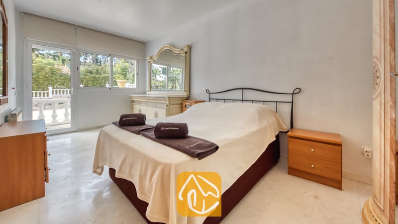 Villas de vacances Costa Brava Espagne - Villa Estrella - Chambre avec lit double, tables de chevet en bois et grandes baies vitrées coulissantes donnant sur une terrasse avec vue sur la verdure.