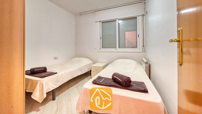 Villas de vacances Costa Brava Espagne - Villa Estrella - Chambre à coucher avec deux lits jumeaux habillés de linge de blanc, une petite table de chevet blanche et une fenêtre avec des stores.