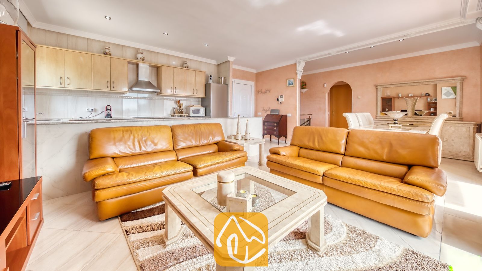 Vakantievilla's Costa Brava Spanje - Villa Estrella - Open-plan woonkamer en keuken in Villa Estrella, voorzien van twee leren banken in een warme zandkleur, een glazen salontafel en lichte houten keukenkastjes.
