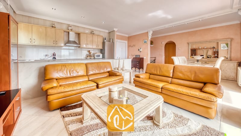 Vakantievilla's Costa Brava Spanje - Villa Estrella - Open-plan woonkamer en keuken in Villa Estrella, voorzien van twee leren banken in een warme zandkleur, een glazen salontafel en lichte houten keukenkastjes.