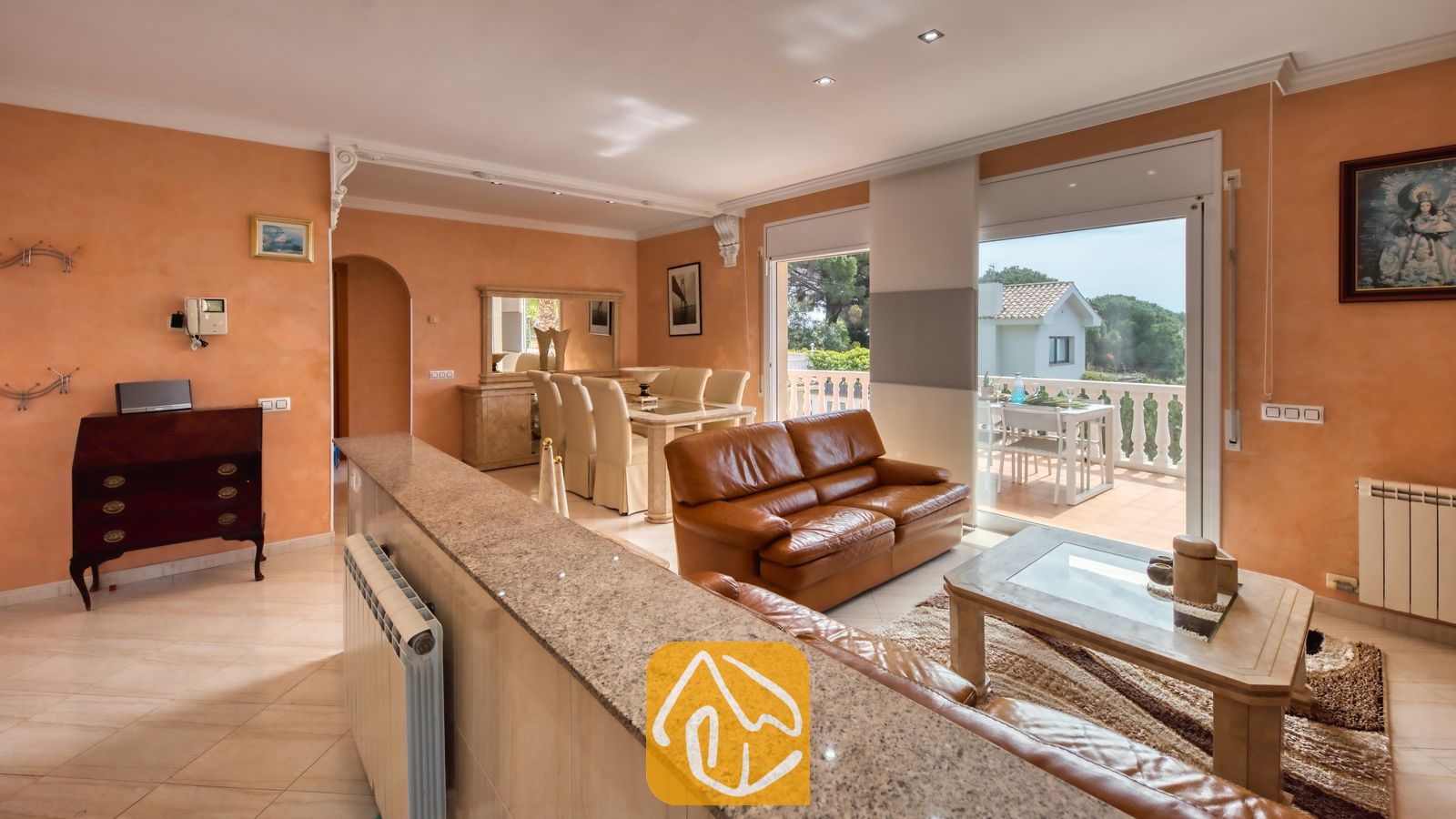 Vakantievilla's Costa Brava Spanje - Villa Estrella - Woonkamer van Villa Estrella met bruine leren banken, een glazen salontafel en perzikleurige muren die uitkomen op een terras.