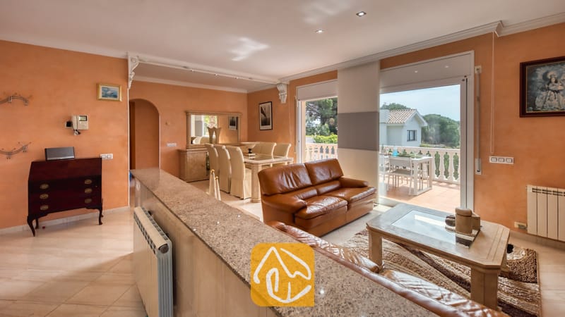 Vakantievilla's Costa Brava Spanje - Villa Estrella - Woonkamer van Villa Estrella met bruine leren banken, een glazen salontafel en perzikleurige muren die uitkomen op een terras.
