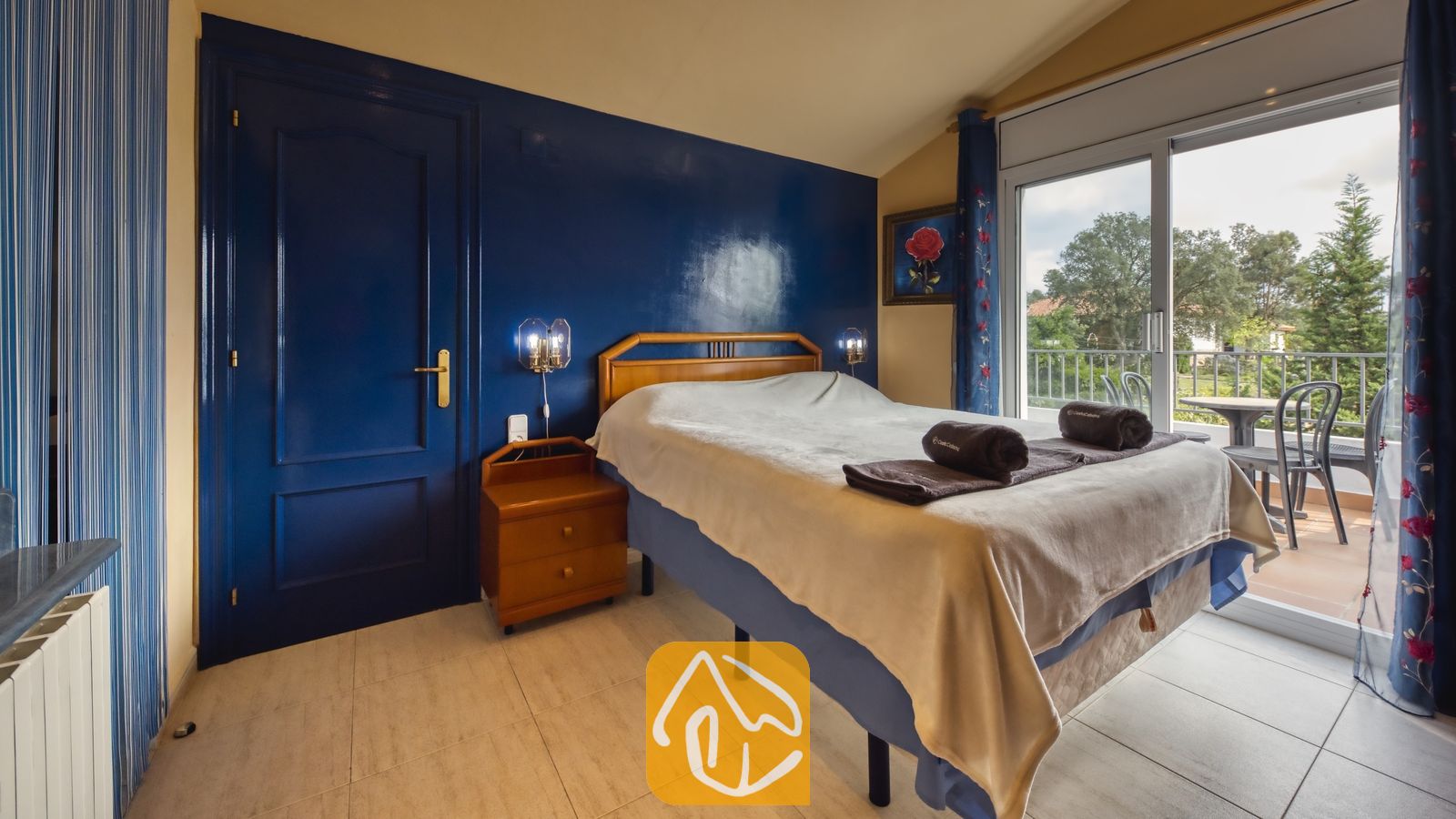 Vakantievilla's Costa Brava Spanje - Villa Geolouk - Slaapkamer met een tweepersoonsbed, een houten nachtkastje en een blauwe accentwand die uitkomt op een balkon bij Villa Geolouk