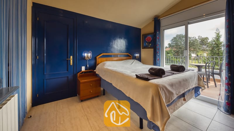 Villas de vacances Costa Brava Espagne - Villa Geolouk - Chambre avec un lit double, une table de chevet en bois et un mur d'accent bleu s'ouvrant sur un balcon à la Villa Geolouk