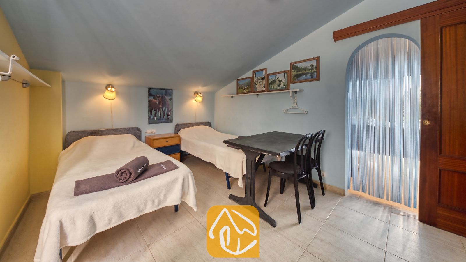 Vakantievilla's Costa Brava Spanje - Villa Geolouk - Slaapkamer met een schuin blauw plafond, twee eenpersoonsbedden met witte spreien, een klein zwart tafeltje met twee stoelen en ingelijste kunst aan de muur.