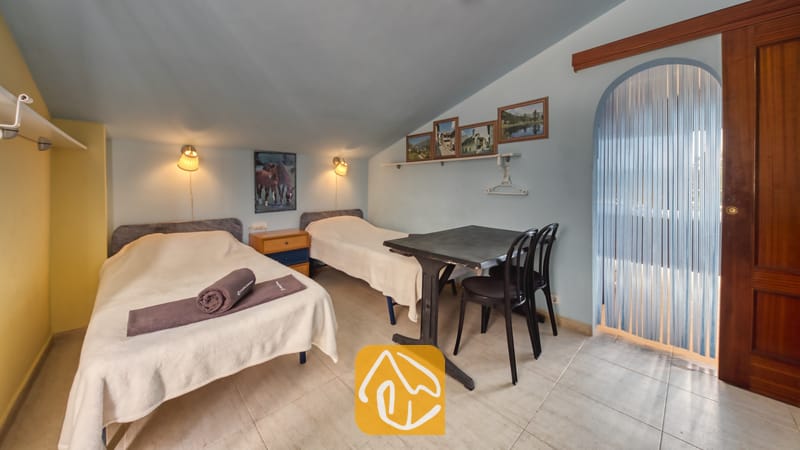 Villas de vacances Costa Brava Espagne - Villa Geolouk - Chambre mansardée aux tons bleus comprenant deux lits simples avec des dessus-de-lit blancs, une petite table noire accompagnée de deux chaises, ainsi que des cadres d'art accrochés au mur.