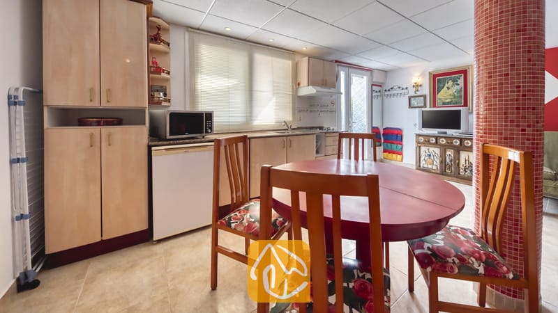 Villas de vacances Costa Brava Espagne - Villa Geolouk - Table de salle à manger ronde en bois rouge avec des chaises à coussins floraux dans la cuisine de la Villa Geolouk, dotée de placards en bois clair et d'une colonne en mosaïque rouge.