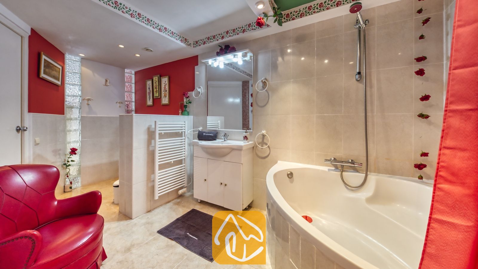 Vakantievilla's Costa Brava Spanje - Villa Geolouk - Badkamer met een hoekbad, een witte wastafel met spiegel en een rood lederen fauteuil tegen rood betegelde muren.