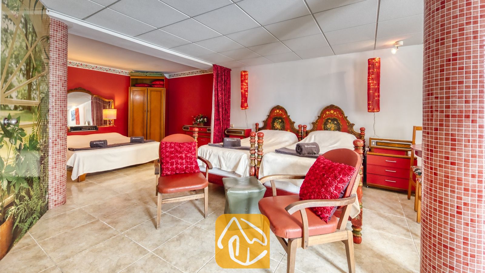 Vakantievilla's Costa Brava Spanje - Villa Geolouk - Slaapkamer met twee eenpersoonsbedden en fraai snijwerk in de houten hoofdborden, rode fauteuils met textielkussens en een tegelvloer.