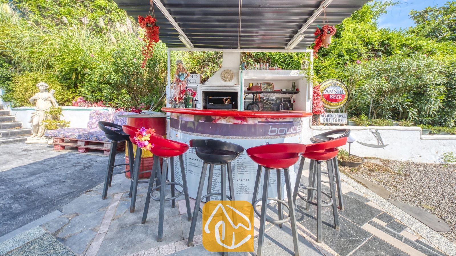 Vakantievilla's Costa Brava Spanje - Villa Geolouk - Buitenbar en grillhoek met rode en zwarte barstoezen, een overkapping en weelderig groen rondom bij Villa Geolouk.
