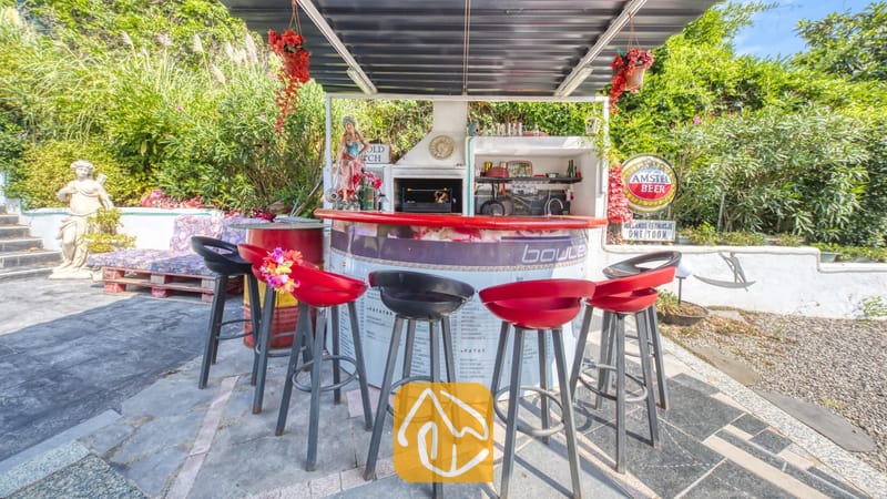 Vakantievilla's Costa Brava Spanje - Villa Geolouk - Buitenbar en grillhoek met rode en zwarte barstoezen, een overkapping en weelderig groen rondom bij Villa Geolouk.