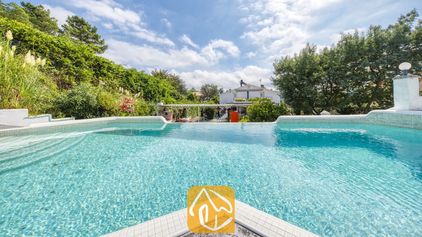 Vakantievilla's Costa Brava Spanje - Villa Geolouk - Privé betegeld zwembad bij Villa Geolouk, omringd door groene bomen, struiken en een blauwe lucht met verspreide wolken.