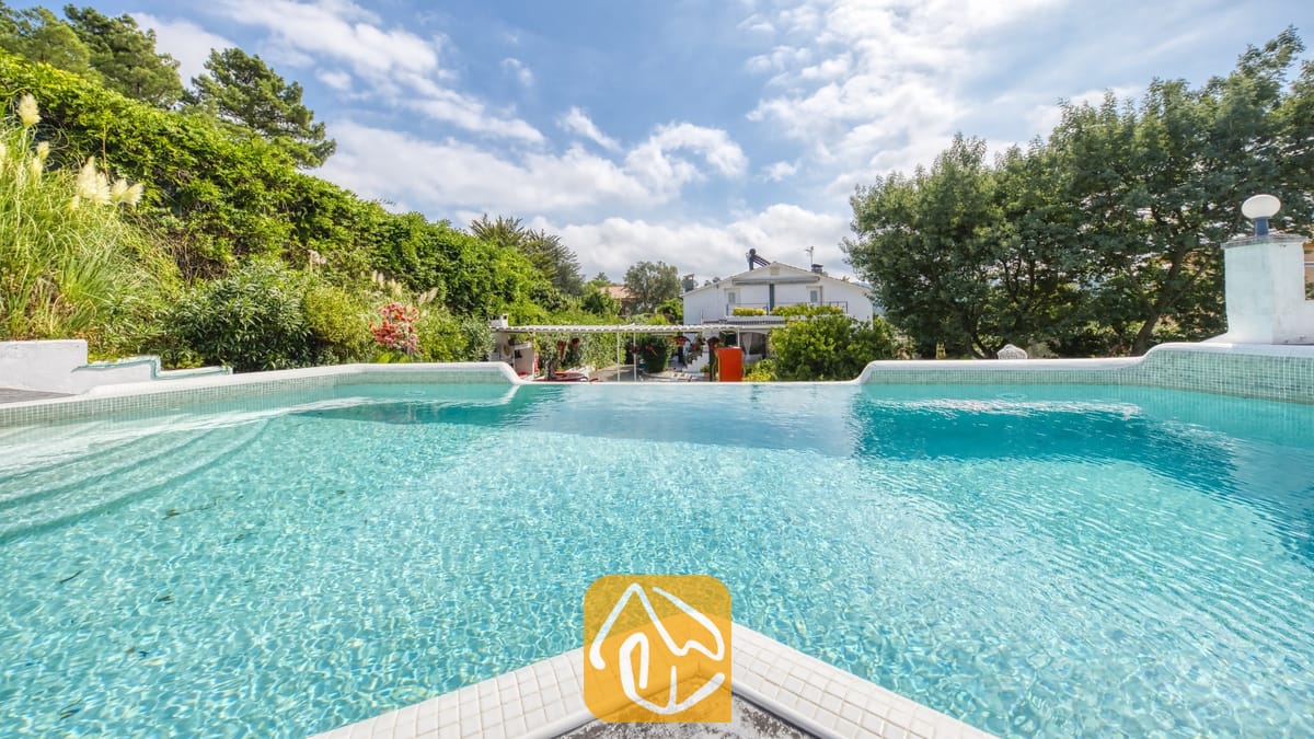 Vakantievilla's Costa Brava Spanje - Villa Geolouk - Privé betegeld zwembad bij Villa Geolouk, omringd door groene bomen, struiken en een blauwe lucht met verspreide wolken.