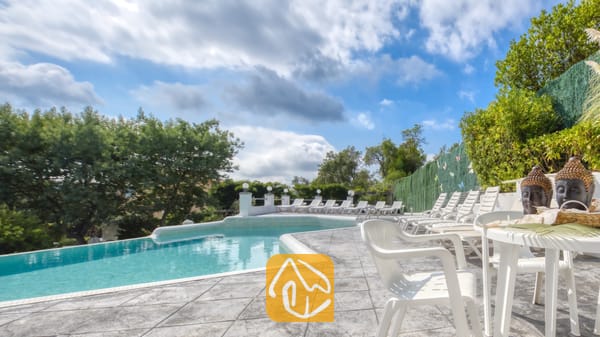 Vakantievilla's Costa Brava Spanje - Villa Geolouk - Privézwembad met betegeld terras en witte kunststof ligstoelen bij Villa Geolouk onder een licht bewolkte hemel.