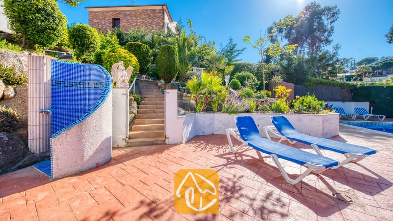 Vakantievilla's Costa Brava Spanje - Villa Jaruco - Terras met buitenzwembad bij Villa Jaruco, voorzien van blauwe ligbedden, een buitendouche met blauwe mozaïektegels en stenen trappen die naar een tuin in verschillende niveaus leiden.