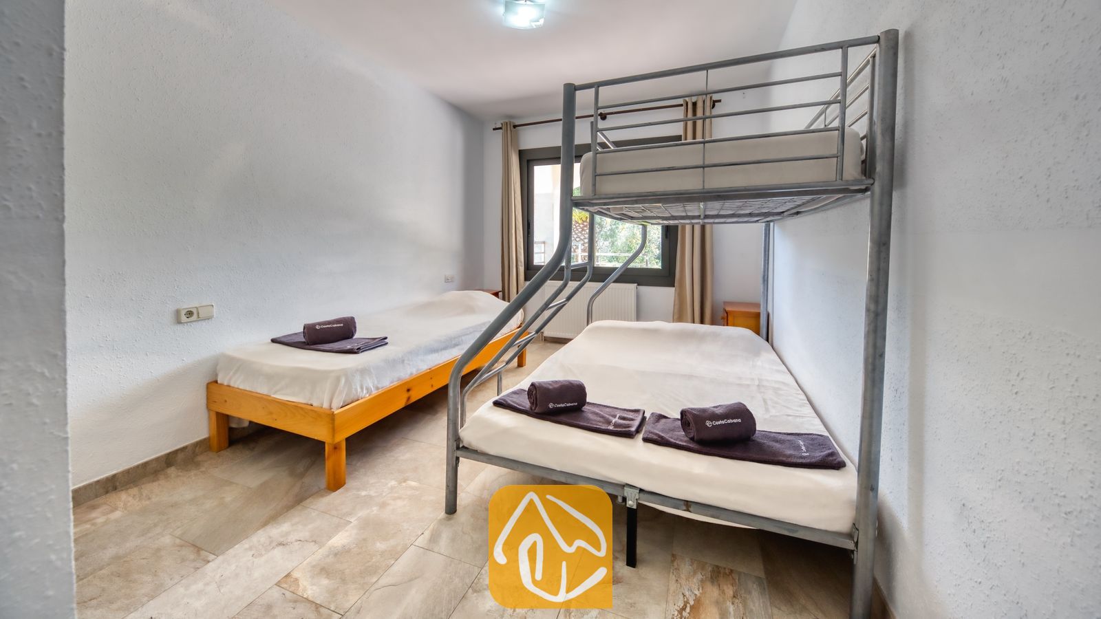 Vakantievilla's Costa Brava Spanje - Villa Jaruco - Slaapkamer met een metalen stapelbed en een apart houten eenpersoonsbed, voorzien van witte muren, tegelvloeren en opgerolde donkere handdoeken op elk matras.