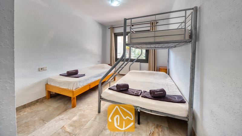 Villas de vacances Costa Brava Espagne - Villa Jaruco - Chambre avec un lit superposé en métal et un lit simple en bois séparé, dotée de murs blancs, de sols carrelés et de serviettes sombres roulées sur chaque matelas.