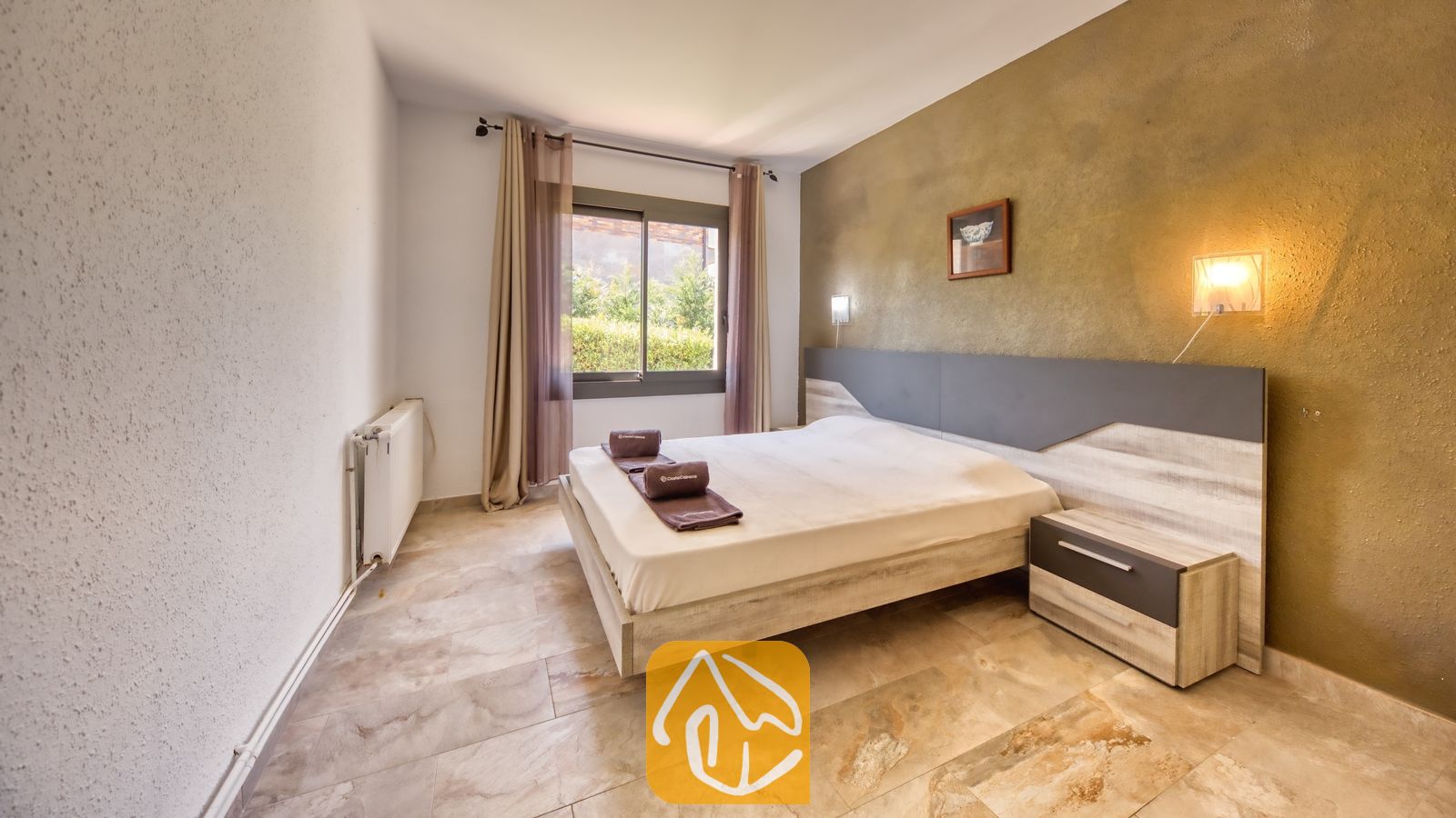 Vakantievilla's Costa Brava Spanje - Villa Jaruco - Slaapkamer met een tweepersoonsbed, een licht houten frame, een bijpassend nachtkastje en een bruine accentmuur met twee wandlampen.