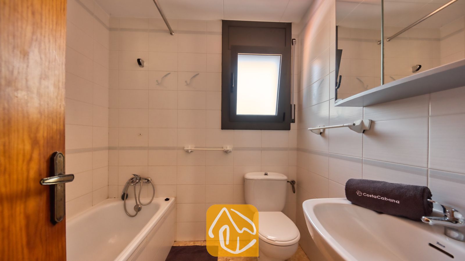 Vakantievilla's Costa Brava Spanje - Villa Jaruco - Badkamer voorzien van een wit ligbad, toilet en wastafel, met betegelde muren en een klein raam met matglas.