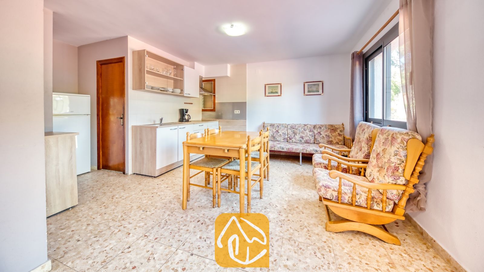 Vakantievilla's Costa Brava Spanje - Villa Jaruco - De open woonkamer en keuken van Villa Jaruco zijn voorzien van een houten eettafel, fauteuils met bloemenprint en terrazzo tegelvloeren.