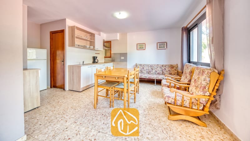 Villas de vacances Costa Brava Espagne - Villa Jaruco - Séjour et cuisine décloordinés à la Villa Jaruco, dotés d'une table à manger en bois, de fauteuils à imprimé floral et d'un sol en carreaux de terrazzo.