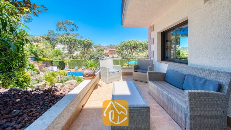 Vakantievilla's Costa Brava Spanje - Villa Jaruco - Terrace van Villa Jaruco, voorzien van grijsvlechwerk tuinameubilair met blauwe kussens, een bijpassende salontafel en uitzicht op een tuin en zwembad.