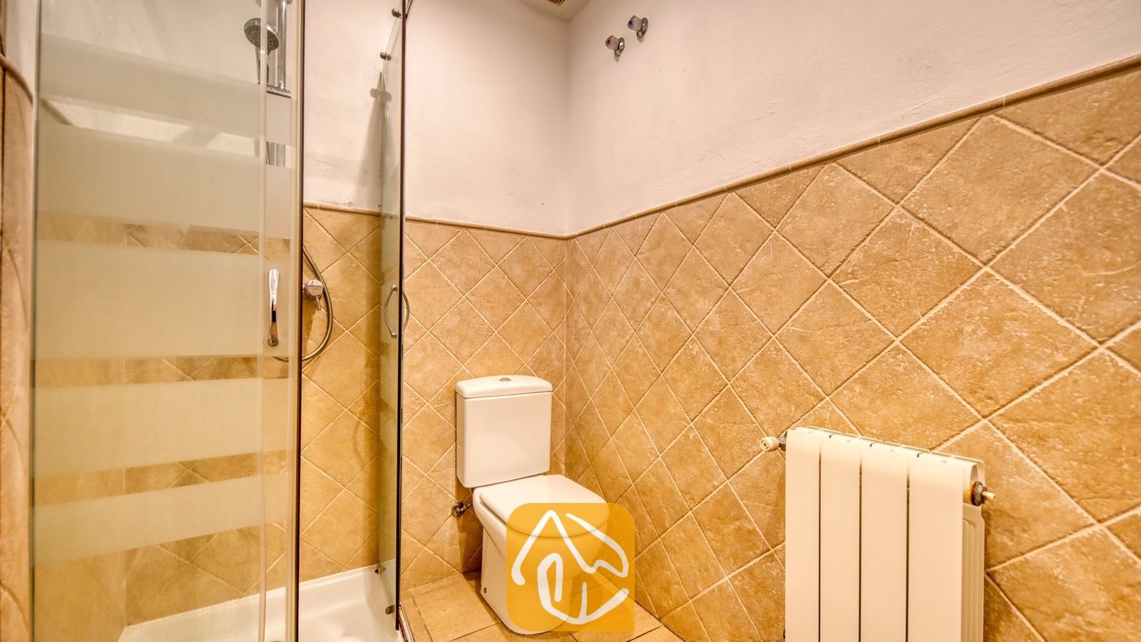 Vakantievilla's Costa Brava Spanje - Villa Marcella - Badkamer voorzien van een wit toilet, glazen douchewand en diagonale, beige wandtegels.