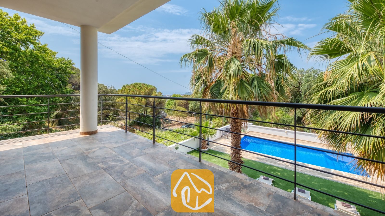 Vakantievilla's Costa Brava Spanje - Villa Marcella - Balkon met grijze natuurstenen tegels en een zwart metalen hekwerk, met uitzicht op het zwembad en de palmbomen van Villa Marcella in Spanje.