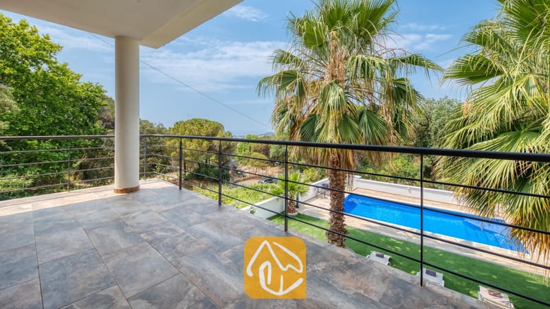 Vakantievilla's Costa Brava Spanje - Villa Marcella - Balkon met grijze natuurstenen tegels en een zwart metalen hekwerk, met uitzicht op het zwembad en de palmbomen van Villa Marcella in Spanje.