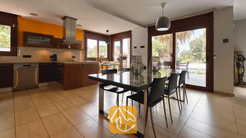 Villas de vacances Costa Brava Espagne - Villa Marcella - Espace repas et cuisine décloqué à la Villa Marcella, doté d'une table avec plateau en verre et chaises noires, de sols en carrelage et de portes coulissantes en verre s'ouvrant sur une terrasse extérieure.