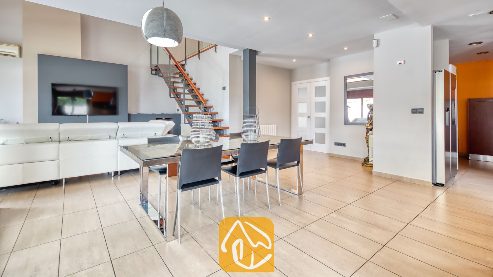 Vakantievilla's Costa Brava Spanje - Villa Marcella - De open woon- en eetkamer van Villa Marcella is voorzien van een glazen eettafel, donkere stoelen, een witte leren bank en een open trap.