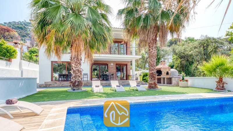 Vakantievilla's Costa Brava Spanje - Villa Marcella - Privézwembad met blauwe mozaïektegels en ligstoelen op het gras bij Villa Marcella, omgeven door palmbomen en voorzien van een stenen barbecue.