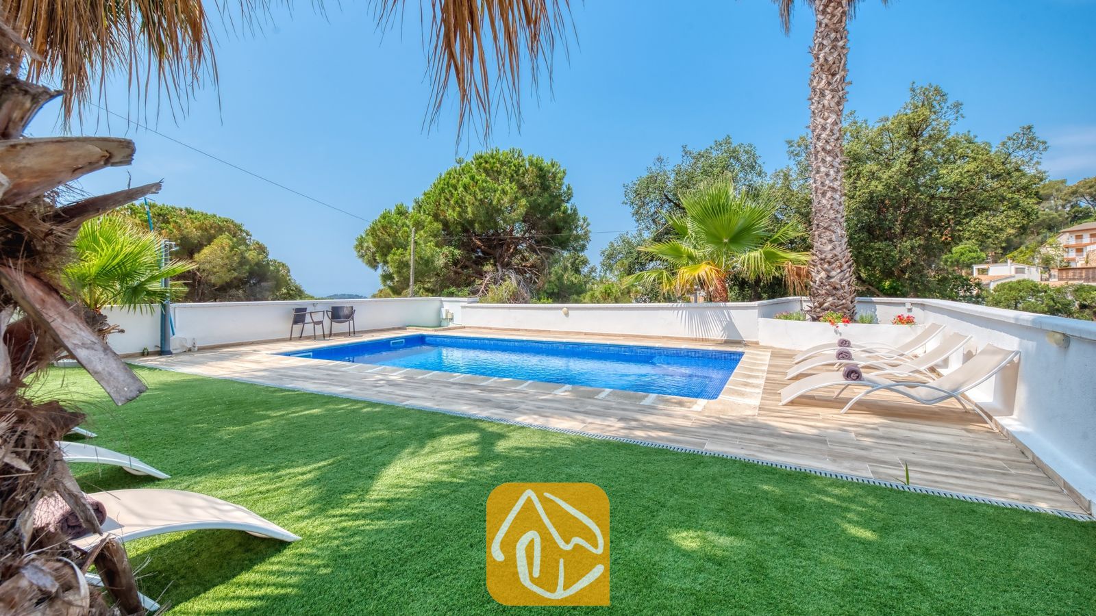 Vakantievilla's Costa Brava Spanje - Villa Marcella - Privézwembad met helderblauw water en beige ligbedden op het betegelde terras van Villa Marcella, omringd door palmbomen en een groen gazon.
