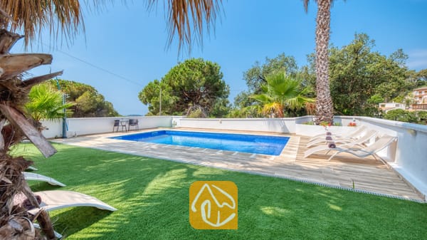 Vakantievilla's Costa Brava Spanje - Villa Marcella - Privézwembad met helderblauw water en beige ligbedden op het betegelde terras van Villa Marcella, omringd door palmbomen en een groen gazon.