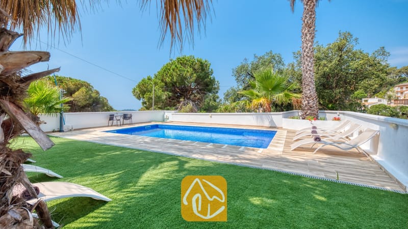 Vakantievilla's Costa Brava Spanje - Villa Marcella - Privézwembad met helderblauw water en beige ligbedden op het betegelde terras van Villa Marcella, omringd door palmbomen en een groen gazon.