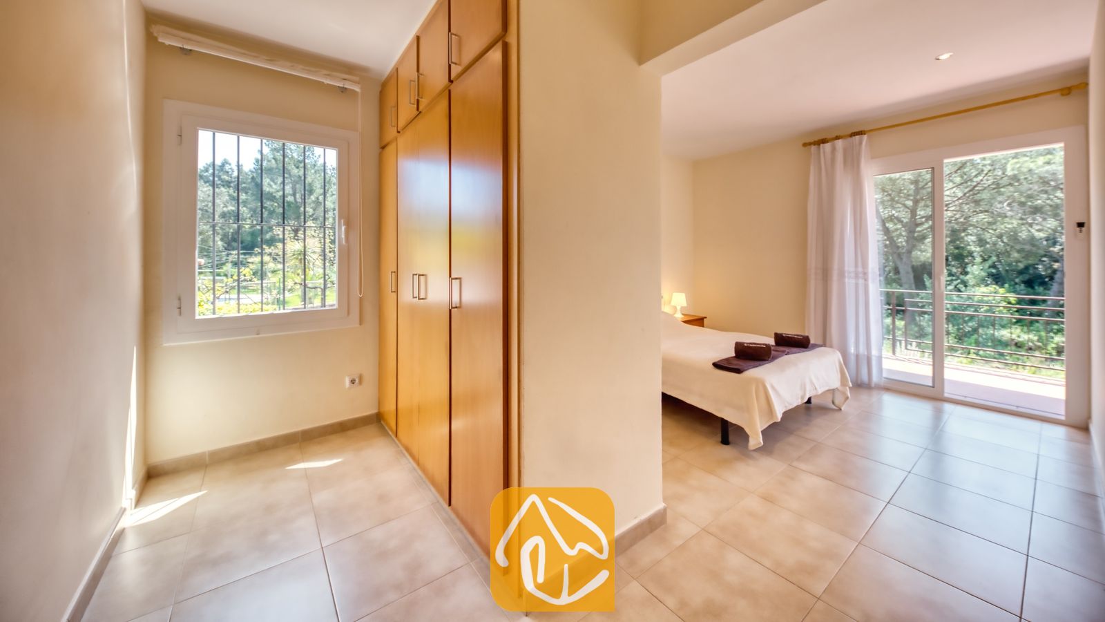 Vakantievilla's Costa Brava Spanje - Villa Lloret - De gang bij de slaapkamers, voorzien van grote houten kledingkasten en een raam aan de linkerkant, leidt naar een slaapgedeelte met een bed en balkondeuren in Villa Lloret.