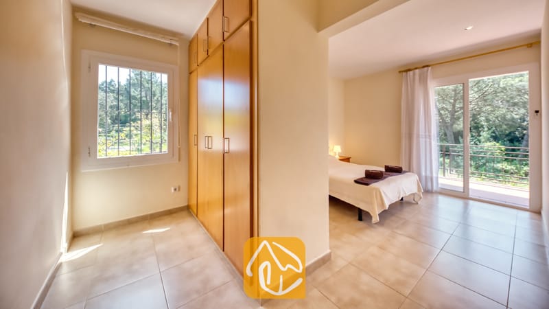 Vakantievilla's Costa Brava Spanje - Villa Lloret - De gang bij de slaapkamers, voorzien van grote houten kledingkasten en een raam aan de linkerkant, leidt naar een slaapgedeelte met een bed en balkondeuren in Villa Lloret.