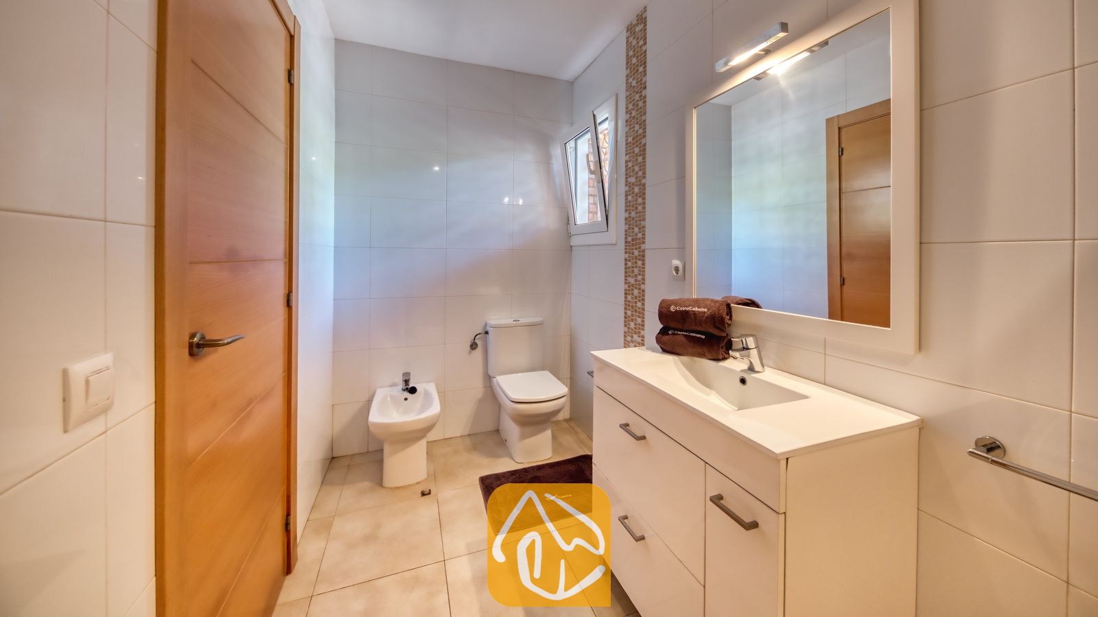 Vakantievilla's Costa Brava Spanje - Villa Lloret - Moderne badkamer met wit betegelde muren, een wit badmeubel met waskom en grote spiegel, een toilet en een bidet.